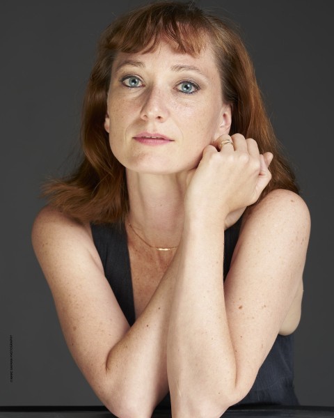 Amanda Treiber, woman with red hair looks towards camera with hands held together towards her left cheek
