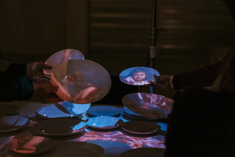 An image of alumni Blue Ka Wing's work 'Peak Hour in the House' screens on plates in an installation