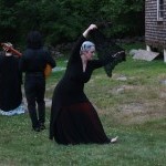 Dancer with a black lace shawl performing outside as two musicians stand nearby.