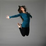 In this image, a woman in blue and black jumps looking towards the sky.