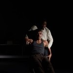 Two men, one supporting the other from behind, holding arms