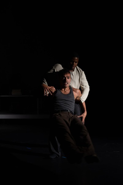 Two men, one supporting the other from behind, holding arms