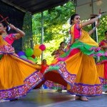 3 women wearing brightly colored dresses twirl on stage at DanceFest