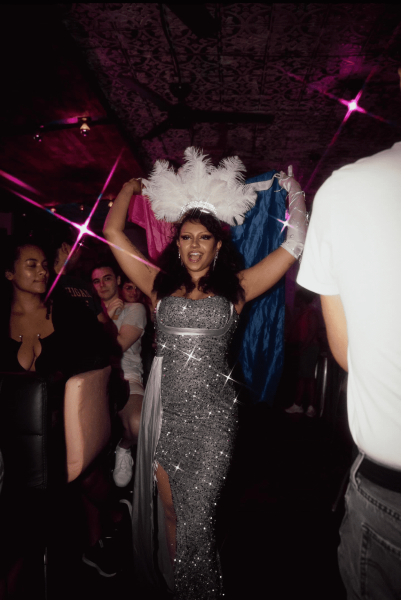 Sparkly showgirl carrying a bisexual Pride flag through an audience aisle.
