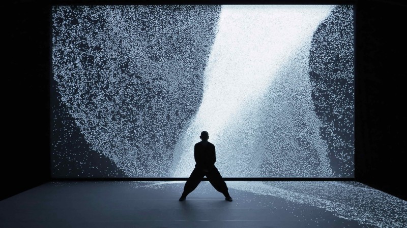 The shadow of Hiroaki in a wide second position in front a large wave of light.