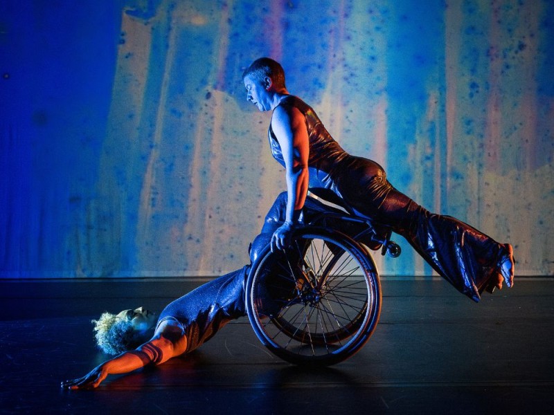  Laurel holds their body in a diagonal line as they balance atop Alice’s wheels and shins. Alice supports from below 