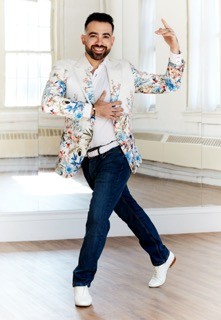 A man standing is a side lunging position with one arm across his chest and one arm out, as if embracing an invisible partner