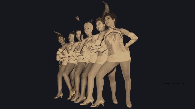 Black and white image of 6 dancers leaning forward with their hands on their hips and right leg bent.