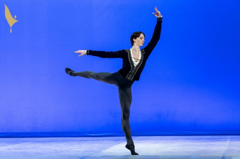  A man dancing in a black leotard and black long-sleeved shirt against a blue background.