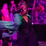 A woman poseswith her right arm bent and gloved hand in front of her face.