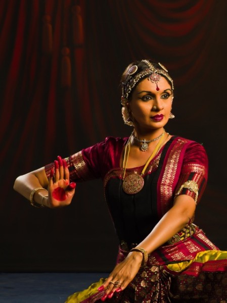 A woman posing in traditional, brightly-colored clothing and gold jewelry.