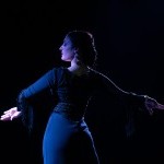 A black and white photo shows a woman, Fanny Ara, in motion, captured from the chest up. She is a flamenco dancer with long dark