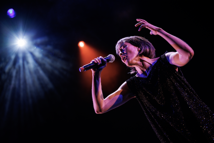 An angled and mid-range shot of a singer’s upper body, rotated at 45 degrees. The singer dramatically sings, holding a mic