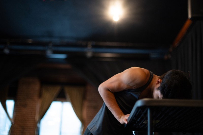 Male-Identifying dancer in front of a curtain, leaning on a black desk.