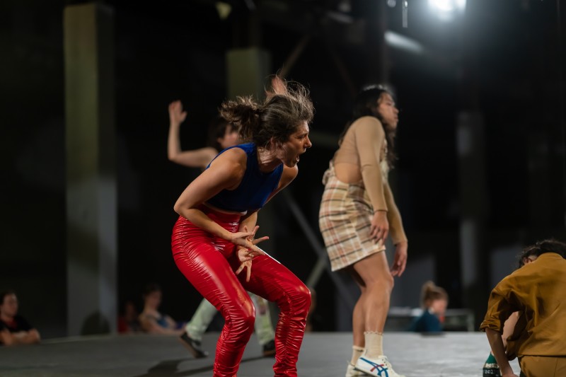 three dancers moving, the front dancer screams in bright red leather pants