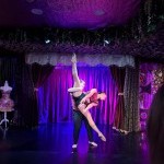 A dancer dressed in black and red is held in a split lift with a second dancer