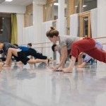 Dance studio with a dancer in red pants in the foreground lunging, and more dancers in the background lunging 