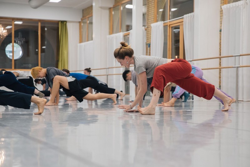 Dance studio with a dancer in red pants in the foreground lunging, and more dancers in the background lunging 