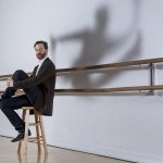 Photo of John Heginbotham with cool shadow of leaping dancer on wall behind him