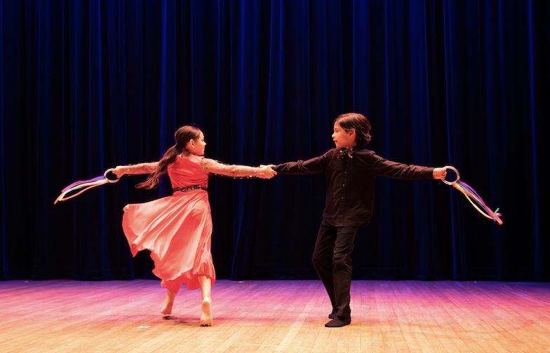 two young dancers holding hands spinning with their other arm extended on stage