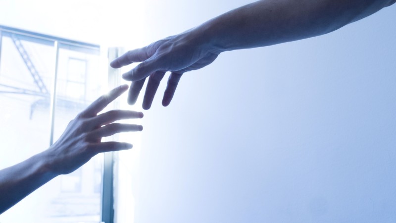 two hands reach towards each other in front of a window