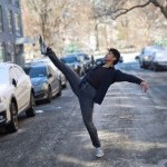 A young man in a dance layout in the middle of a New York street in every day clothing.