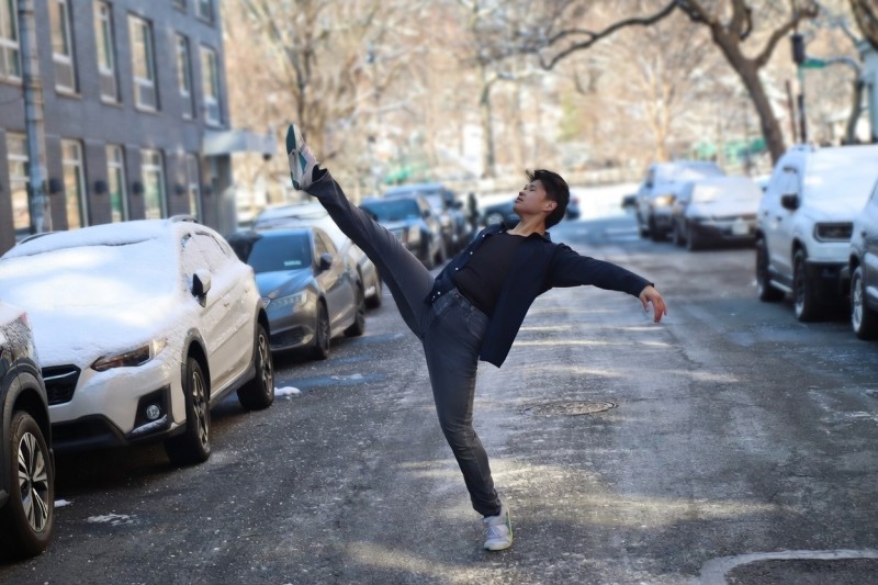 A young man in a dance layout in the middle of a New York street in every day clothing.