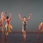 Four women dance and look up at the sky with their arms above their heads, palms open towards the ceiling.
