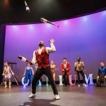 Woman hanging by hair in a split performing on stage.