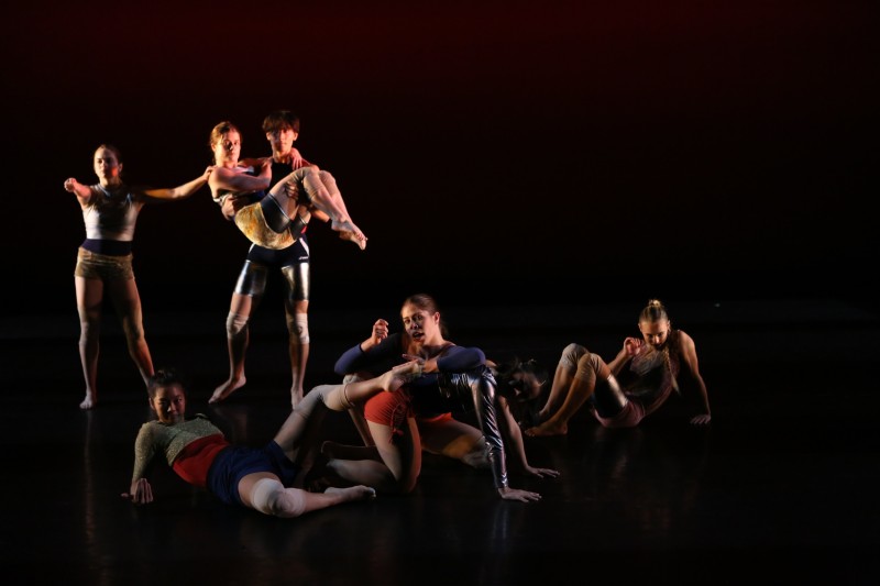 a group of seven dancers in strange poses looking at an imaginary TV