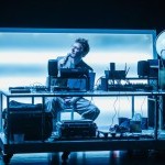 A man with glasses sitting at his desk and holding a mic.
