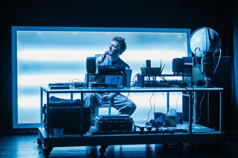 A man with glasses sitting at his desk and holding a mic.