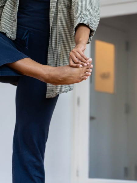 Black person wearing navy and green standing on one leg, left arm holding right big toe across the center of their body.