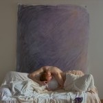 Male dancer slumped over an all white couch with a lavender backdrop and violets on the floor.