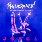 A dancer, lifted by another dancer, reaches towards the sky with her hands and feet extended.