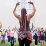 Female identifying dancer holding her arms up while teaching a large crowd of young students