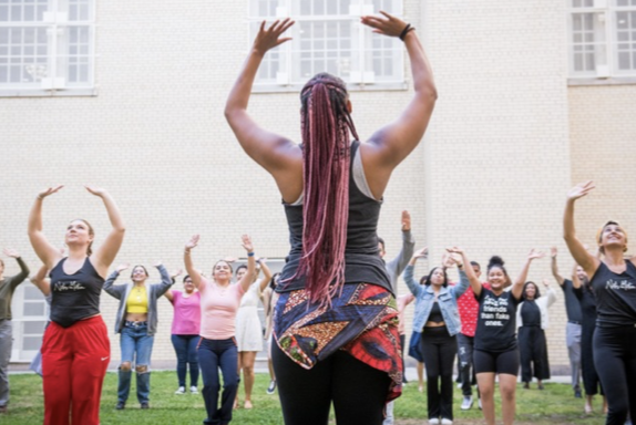 Female identifying dancer holding her arms up while teaching a large crowd of young students
