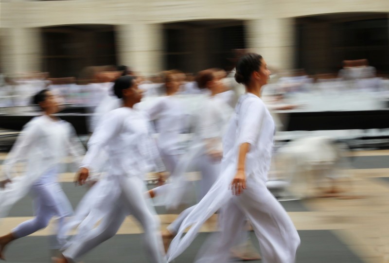 Outdoor plaza; blurred image of multiple dancers running wearing white cotton tunics and leggings