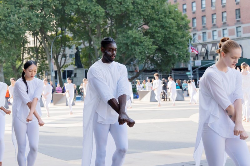3 Dancers in white on outside plaza, arms crossed at the wrist