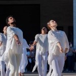 3 Dancers in white on outside plaza, arms crossed at the wrist