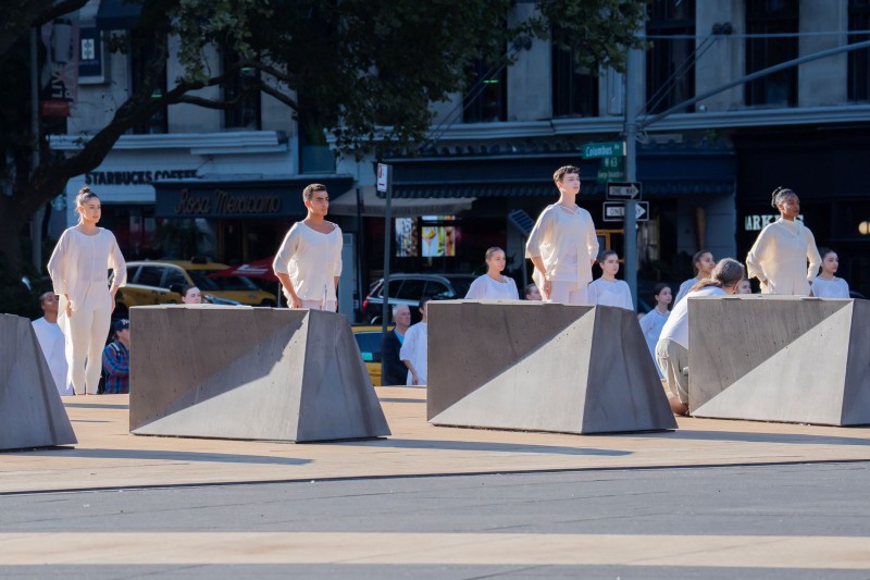 3 Dancers in white on outside plaza, arms crossed at the wrist