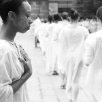 Dancers in white, side by side, arms folded against clasping a white plate