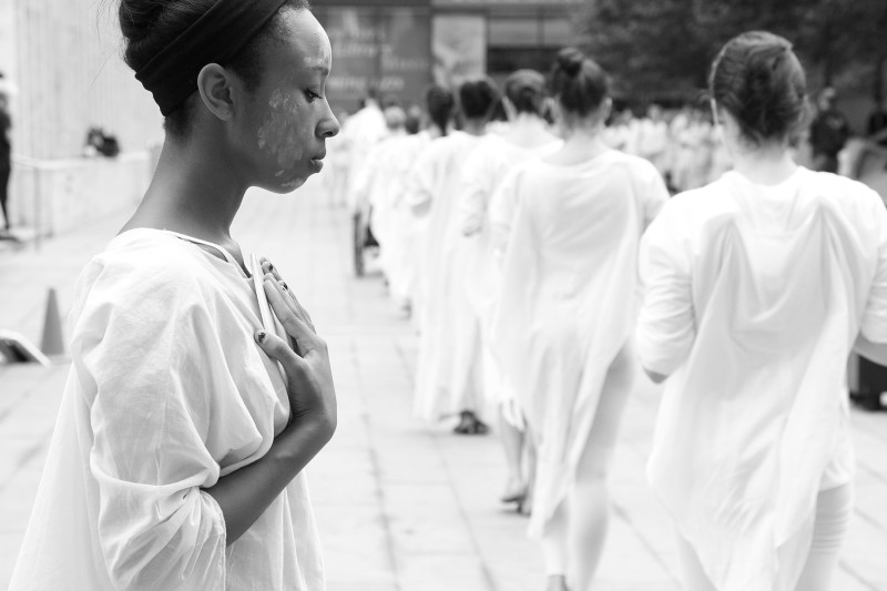 Dancers in white, side by side, arms folded against clasping a white plate