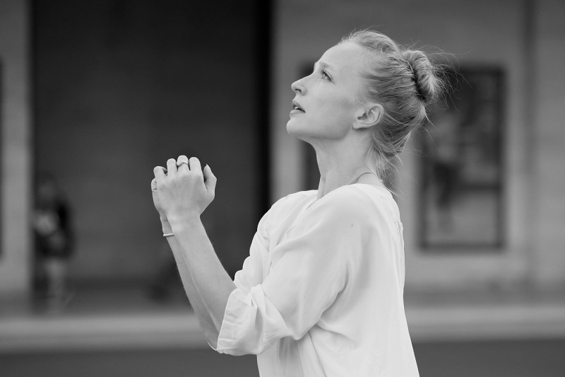 Dancers in white, blond hair in a high bun, hands clasped in prayer 