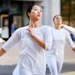 Dancers in white clasping a white ceramic plate to their chest, encircling an outdoor plaza
