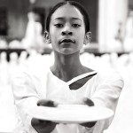 Dancer in white, black hair pulled back offering a white ceramic plate