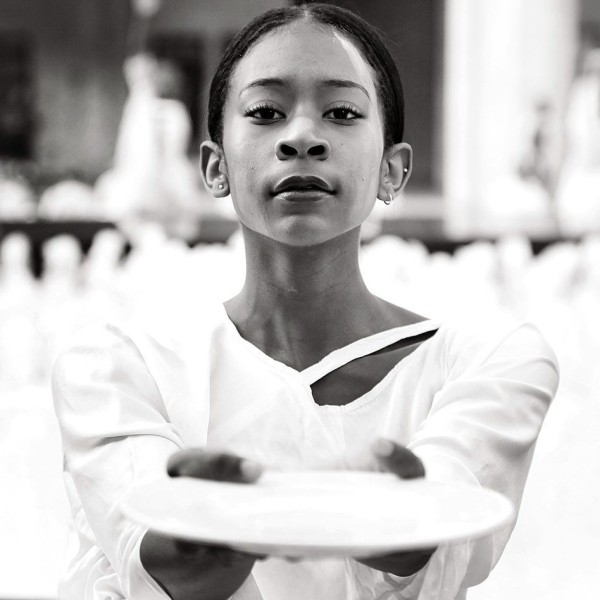 Dancer in white, black hair pulled back offering a white ceramic plate
