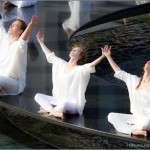 Dancers in white sitting cross-legged on rim of fountain with arms upraised