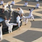 multiple dancers in white around a circular black marble fountain