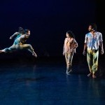 1 dancer leaping and 2 standing facing front with heads turned towards the dancer who is leaping